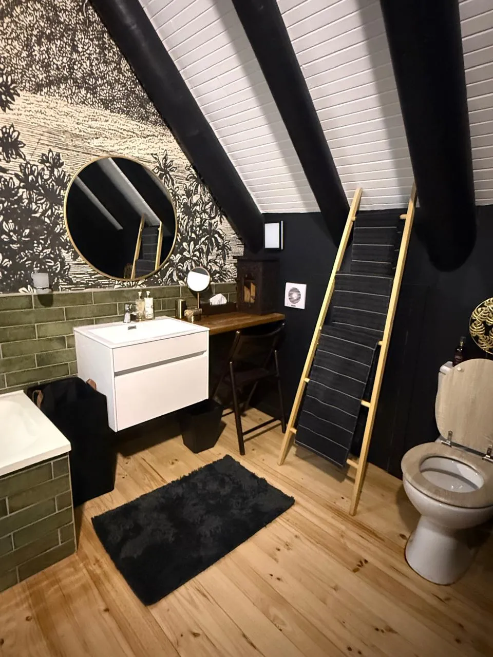The bathroom with botanical feature wallpaper, sage green subway tiles and a round gold-framed mirror