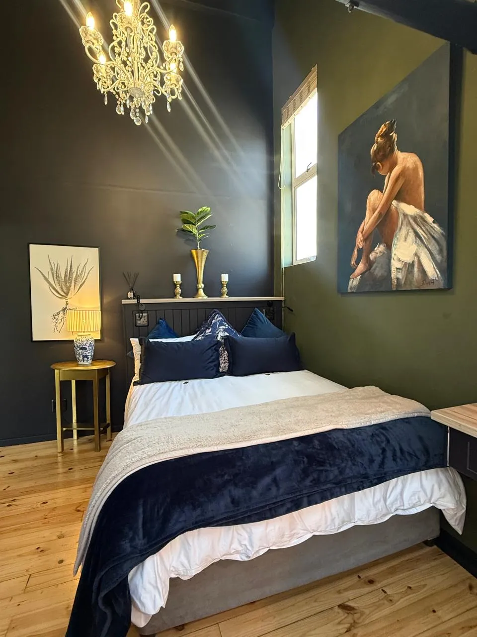 The double bedroom with a crystal chandelier, deep green walls and a large figurative canvas