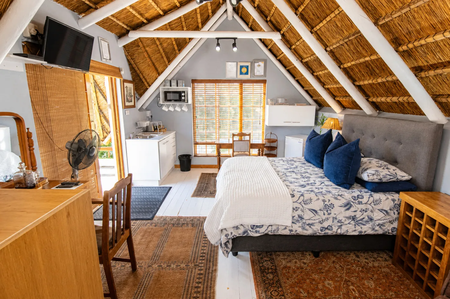 Berry Cottage's queen bed and kitchenette together beneath the vaulted thatch ceiling