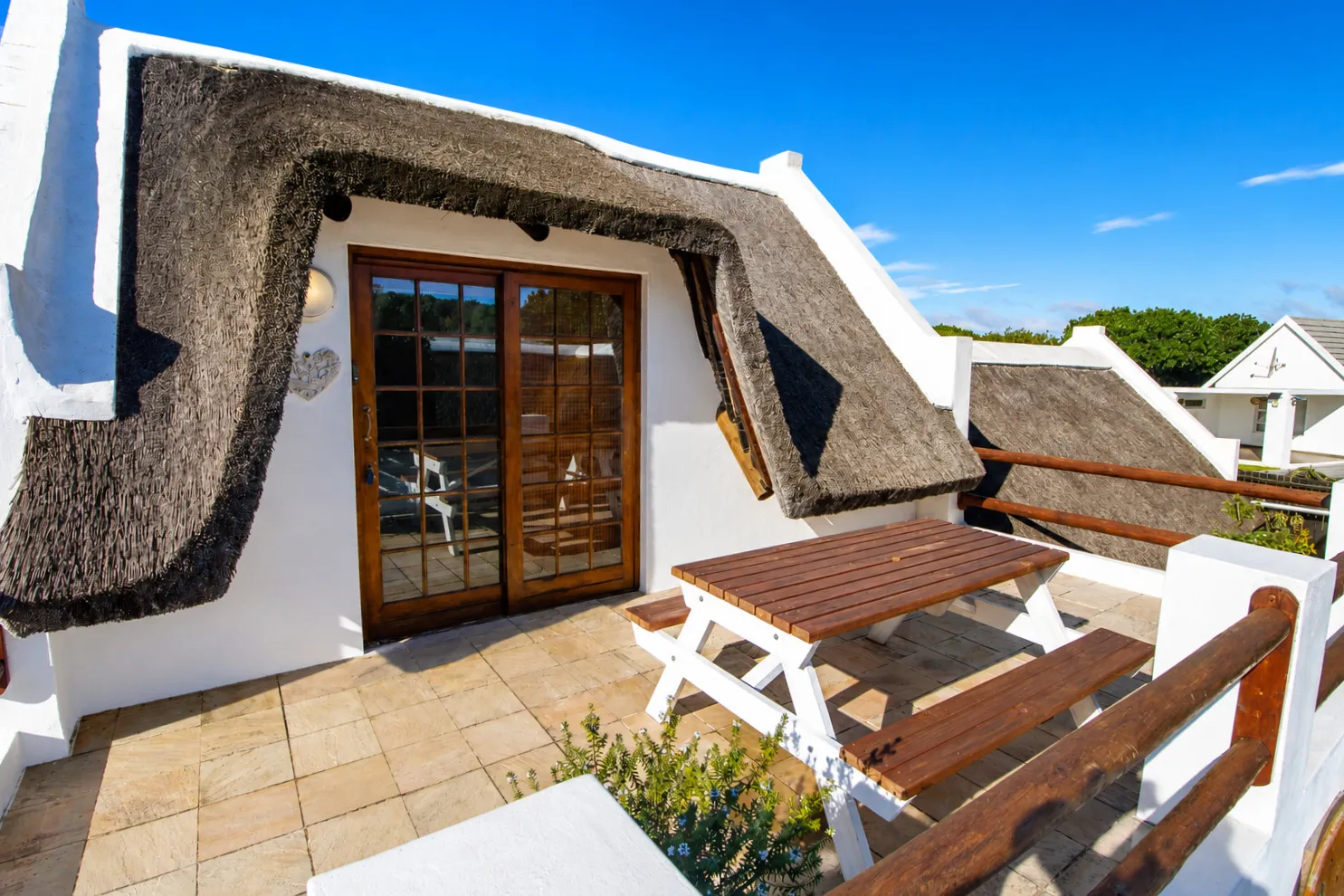 Berry Cottage's verandah at ground level, with a picnic table beneath the thatch overhang
