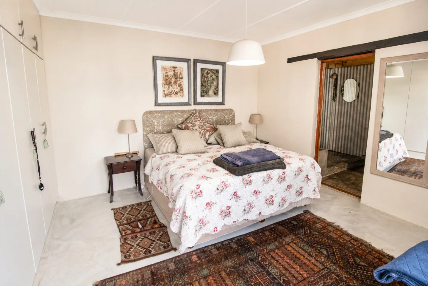 A double bedroom with a patterned floral bedspread, opening through to the en-suite bathroom