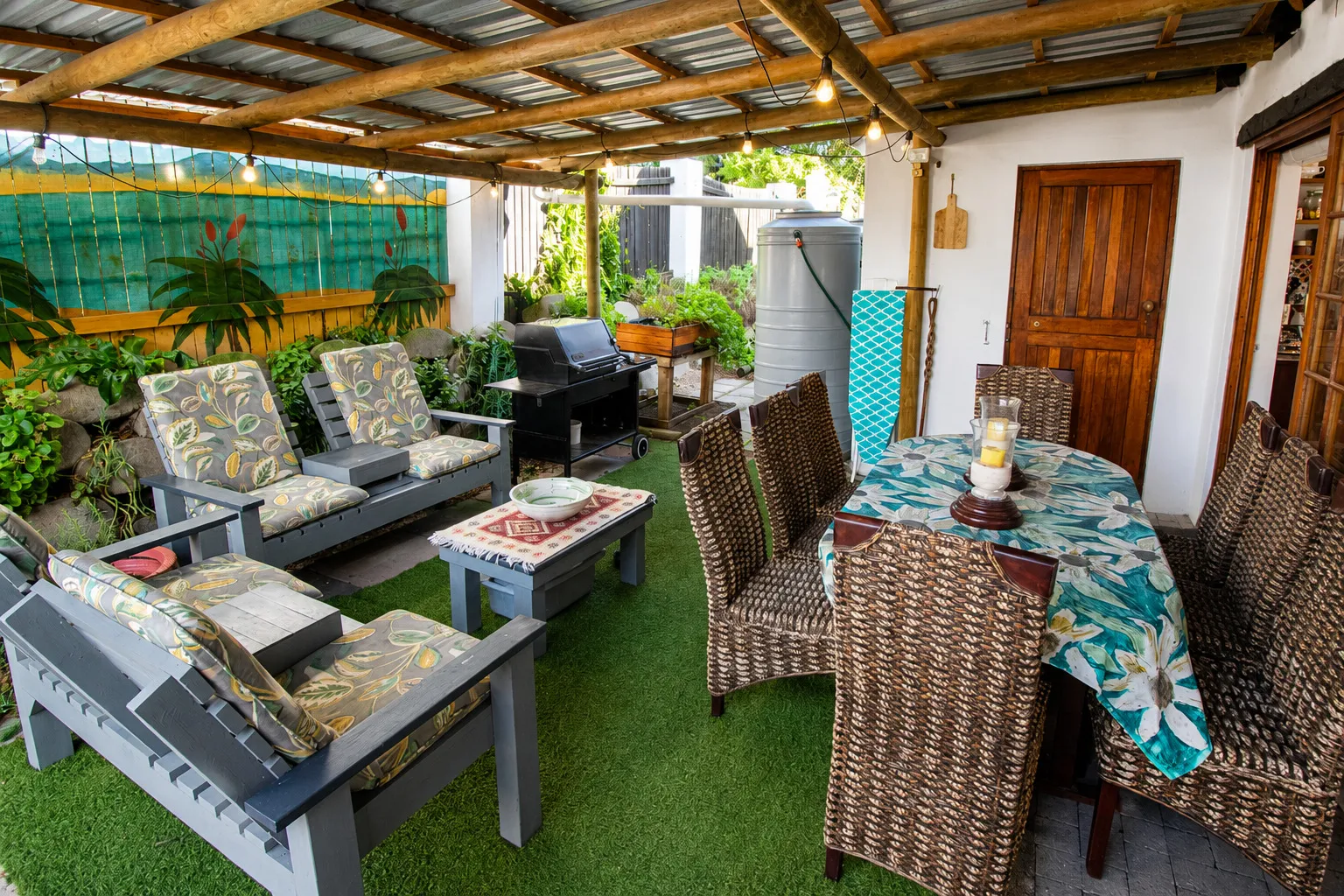The covered braai area with wicker dining chairs and a mural-painted screen wall