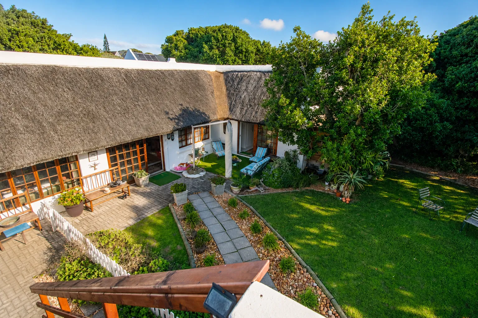 Aerial view over the back garden and patio, with loungers, lawn and mature trees