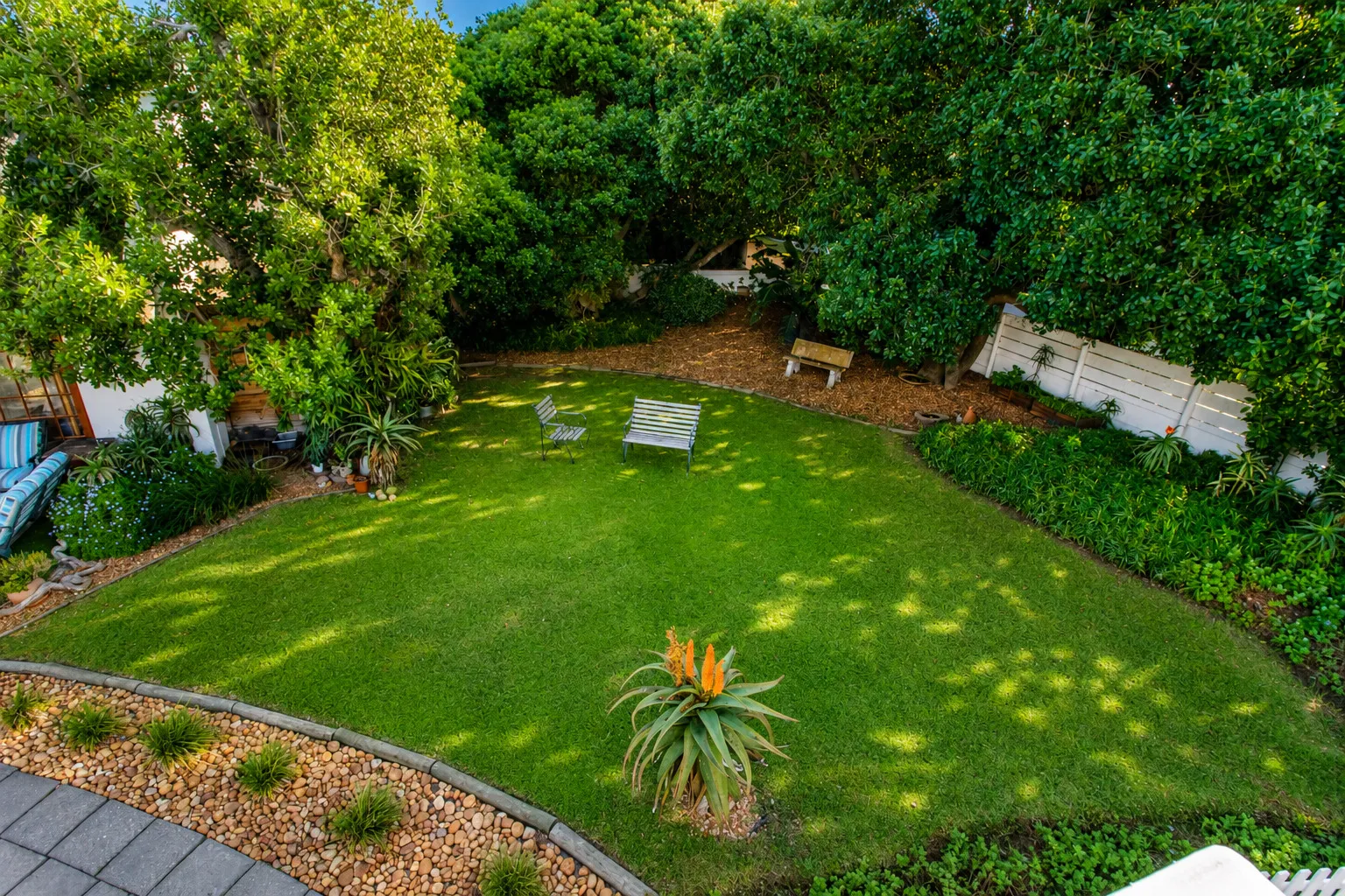 A second aerial view of the back garden, bordered by hedges and a white timber fence