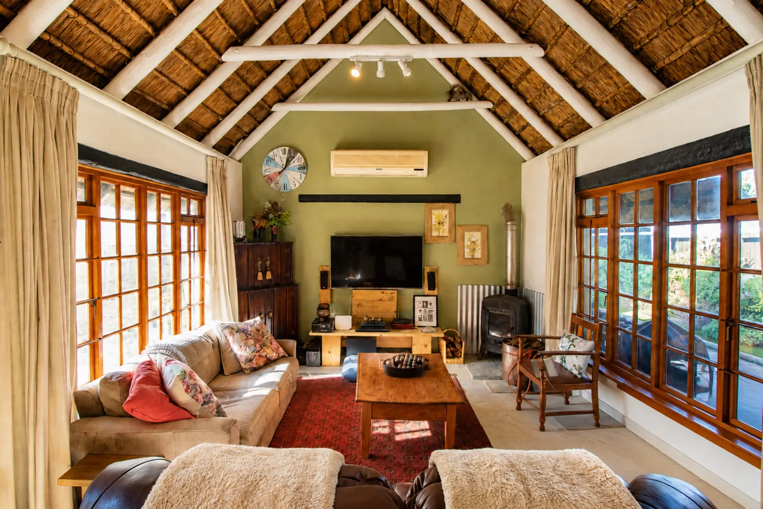 The lounge beneath the thatch, with leather sofas, a wood-burning stove and views through the windows to the garden