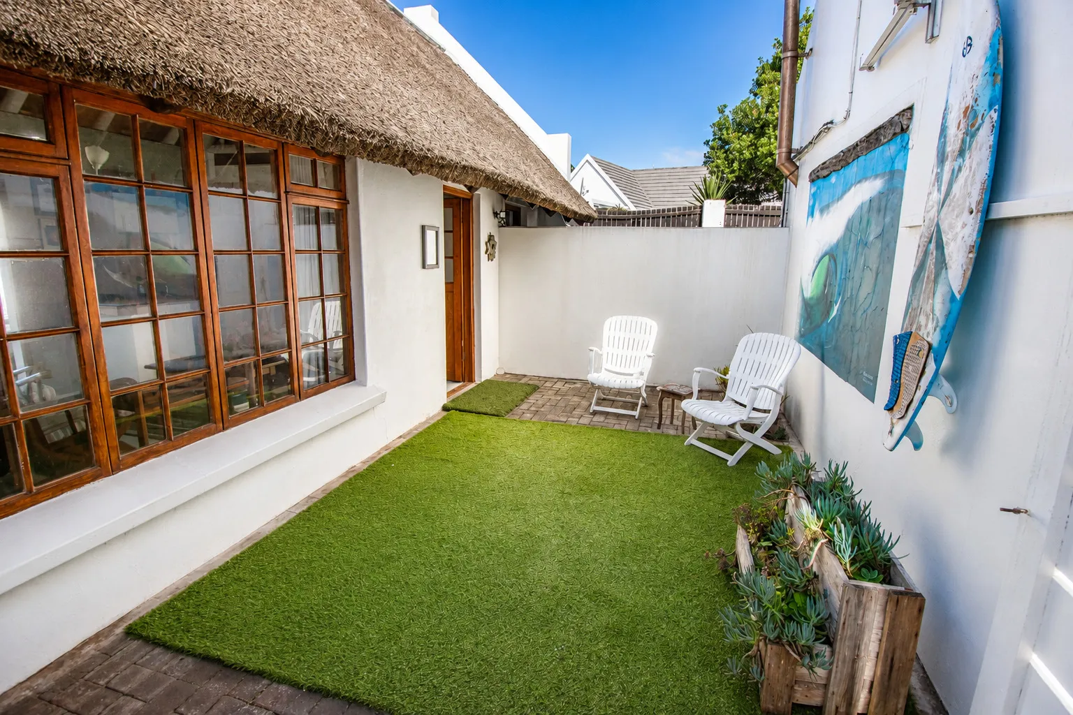 Milkwood Cottage's private courtyard, with deck chairs and surfboard art against the whitewashed wall